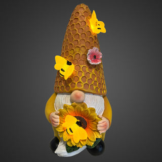 Gartenfigur eines Wichtels mit Sonnenblume und honigwabenartiger Mütze mit Bienen, Solar‑LED, 18 cm hoch. Beleuchtet mit grauen Hintergrund
