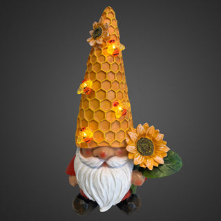 Gartenfigur eines Wichtels mit großer Sonnenblume und honigwabenartiger Mütze mit Bienen, Solar‑LED, 30 cm hoch.Beleuchtet mit grauen Hintergrund