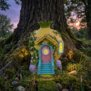 Gartenfigur „Wichtelhaus“ (ca. 21 cm) mit Solar-LED, gelbes Rundhaus mit grünem Dach, rosa Tür und leuchtenden Fenstern, dekoriert mit Blumenranken. Steht auf moosigem Boden am Fuß eines Baumes bei Dämmerung.