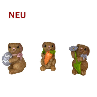 Drei farbige 8‑cm‑Osterhasenfiguren, jeweils mit einem Ei, einer Möhre und einer Blume in den Pfoten.