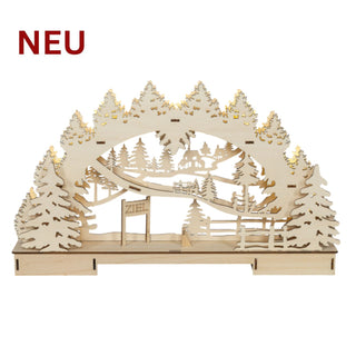 Naturfarbener Bausatz für einen LED‑Schwibbogen aus Holz (ca. 45 cm) mit detailreicher Wald- und Winterszene unter einem geschwungenen Bogen; im Motiv sind Tannenbäume, ein Haus, Zäune und ein Schild mit der Aufschrift „ZIEL“ zu sehen.