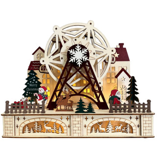 Holzdeko mit großem beleuchtetem Riesenrad in winterlicher Weihnachtslandschaft mit Häusern, Tannenbäumen, Rentier, Weihnachtsmannfigur und dekorativen Hirschmotiven im Sockel; warm beleuchtete Fenster im Hintergrund.