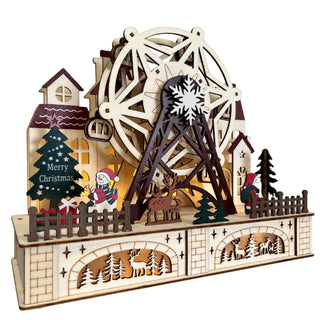 Holzdeko in Form einer weihnachtlichen Landschaft mit großem beleuchtetem Riesenrad, Häusern, Tannenbäumen, Rentier, Weihnachtsfigur und filigranen Hirschmotiven im unteren Sockel; seitliche Perspektive mit warmem Licht.