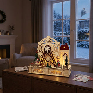 LED-Riesenrad-Mini (28 cm) mit Musik, farbige Holzszene mit drehbarem Riesenrad, Häusern und Figuren, warm beleuchtet auf einer Kommode vor winterlicher Fensterkulisse platziert.