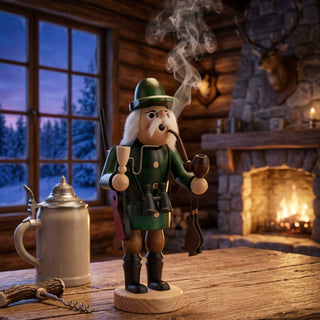 Farbiges Räuchermännchen „Jäger“ (32 cm) aus Holz. Die Figur trägt eine grüne Jagduniform mit Hut, hält eine Pfeife und ein erlegtes Wildtier. Ein Gewehr ist auf dem Rücken befestigt, ein Fernglas hängt vor der Brust. Aus dem geöffneten Mund steigt Rauch auf. Das Räuchermännchen steht auf einem Holztisch in einer rustikalen Jagdhütte vor einem Kaminfeuer, daneben befinden sich ein Bierkrug und Jagdzubehör. Im Hintergrund ist durch ein Fenster eine winterliche Waldlandschaft zu sehen.