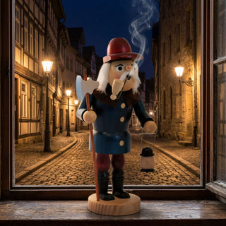Farbiges Räuchermännchen „Nachtwächter“ (30 cm) aus Holz. Die Figur trägt einen roten Hut, einen dunkelblauen Mantel, rote Hosen und schwarze Stiefel. In der linken Hand hält der Nachtwächter eine Hellebarde, in der rechten eine Laterne. Aus der Pfeife im Mund steigt Rauch auf. Die Figur steht auf einer Fensterbank vor einer historisch anmutenden Altstadtgasse mit Kopfsteinpflaster und beleuchteten Straßenlaternen bei Nacht.