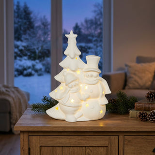LED-Weihnachtsbaum mit Schneemännern (18 cm), weiße Keramik mit warm leuchtenden Sternausschnitten, dekorativ auf einer Kommode vor winterlicher Fensterkulisse platziert.