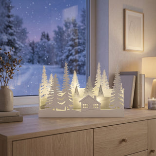 LED Diorama „Winterwald“ (30 cm), warmweiß beleuchtet mit Timerfunktion, filigrane Silhouetten aus Bäumen und einer Hütte in weißer Optik, stimmungsvolle Winterdekoration vor verschneiter Fensterlandschaft im Wohnraum.