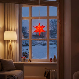 LED Adventsstern von HGD in Rot mit einem Durchmesser von 12 cm. Der beleuchtete Stern hängt an einer Schnur vor einem Fenster und strahlt ein warmes rotes Licht aus. Im Hintergrund ist eine winterliche Schneelandschaft zu sehen, während der Innenraum mit einer Stehlampe, einem Sessel und weihnachtlicher Dekoration auf der Fensterbank gemütlich gestaltet ist. Der batteriebetriebene Stern mit Timerfunktion eignet sich als stimmungsvolle Weihnachtsdekoration für Fenster und Wohnräume.