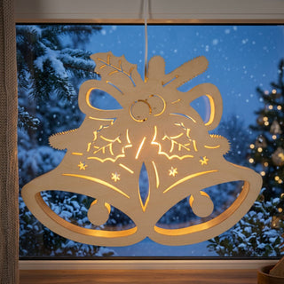 LED‑Fensterbild in Form einer Glocke aus naturfarbenem Holz, warm beleuchtet und am Fenster aufgehängt. Die filigranen Ausschnitte zeigen Schleife, Tannenzweige und Sterne; im Hintergrund ist eine verschneite Winterlandschaft mit Bäumen und einem geschmückten Weihnachtsbaum zu sehen.