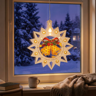 LED‑Fensterbild in Sternform aus naturfarbenem Holz mit farbig gestalteten Glocken, warm beleuchtet und am Fenster aufgehängt. In der Mitte hängen zwei gelbe Glocken mit roter Schleife und Tannengrün, umgeben von leuchtenden Sternen. Im Hintergrund ist eine verschneite Winterlandschaft bei Nacht zu sehen; im Innenraum befinden sich eine Tasse, Bücher und eine Decke auf der Fensterbank.