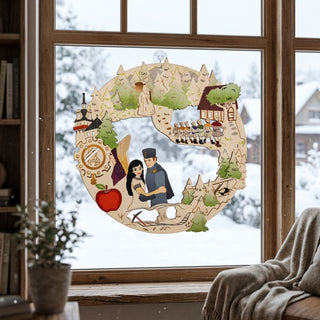 Fensterbild aus Holz mit Motiv „DEFA‑Schneewittchen“, bunt abgesetzt und am Fenster aufgehängt. Das runde Design zeigt eine zentrale Szene mit zwei Figuren in der Mitte, umgeben von Märchenelementen wie den sieben Zwergen, einem Wald mit Tannen, einem kleinen Haus, einem Schloss und dem roten Apfel. Das Fensterbild hängt vor einer verschneiten Winterlandschaft; im Innenraum sind ein Sessel mit Decke und eine Pflanze auf der Fensterbank zu sehen.

