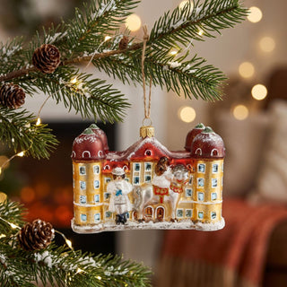 Christbaumschmuck „Drei Haselnüsse für Aschenbrödel®“ mit Motiv von Schloss Moritzburg. Der detailreiche Weihnachtsanhänger hängt an einem festlich dekorierten Tannenzweig mit Lichterkette.