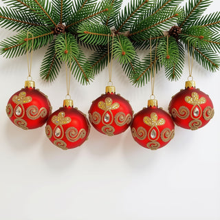 Fünf rote Christbaumkugeln aus Glas hängen an einem grünen Tannenzweig. Die Kugeln sind mit goldfarbenen Glitzerornamenten, filigranen Perlenlinien und klaren, tropfenförmigen Schmucksteinen verziert. Die geschwungenen Muster und funkelnden Details bilden einen eleganten Kontrast zur roten Oberfläche. Das 5-teilige Christbaumschmuck-Set verleiht dem Weihnachtsbaum eine festliche und luxuriöse Rot-Gold-Optik.