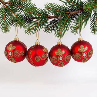 Vier rote Christbaumkugeln aus Glas hängen an den Zweigen eines Tannenbaums. Die matt roten Kugeln sind mit goldfarbenen Glitzerornamenten, filigranen Perlenlinien und geschwungenen Mustern verziert. Klare, tropfenförmige Schmucksteine setzen edle Akzente und unterstreichen die festliche Rot-Gold-Kombination. Das 4-teilige Set wirkt elegant, hochwertig und besonders weihnachtlich.