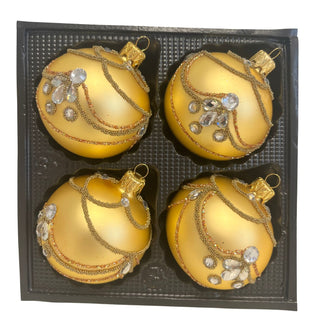 Vier goldfarbene Christbaumkugeln aus Glas in einer schwarzen Verpackungseinlage. Die Kugeln sind matt gold beschichtet und mit aufwendigen goldenen Perlenbändern, feinem Glitterdekor sowie klaren, facettierten Schmucksteinen verziert. Die luxuriöse Verzierung verläuft in geschwungenen Linien über die gesamte Oberfläche und verleiht dem 4-teiligen Christbaumschmuck-Set einen eleganten, opulenten Charakter.