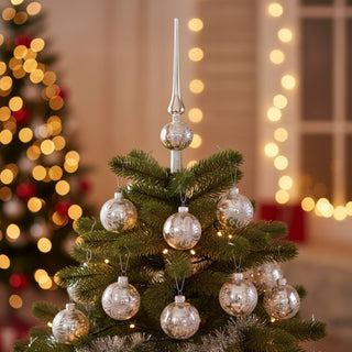 Christbaumschmuck „Silber“ aus Glas im 16-teiligen Set, bestehend aus silbernen Glaskugeln mit feinem Dekor und passender Baumspitze, dekorativ am Weihnachtsbaum verteilt, umgeben von grünen Tannenzweigen und warm leuchtenden Lichtern im Hintergrund.