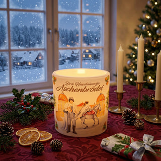 Windlicht aus Wachs „Drei Haselnüsse für Aschenbrödel®“ mit Teelicht und farbigem Filmmotiv. Das leuchtende Windlicht steht auf einer festlich dekorierten Weihnachtstafel vor einem verschneiten Fenster.