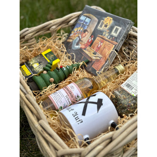 Präsentkorb „Himmelfahrt“ von SAICO mit geflochtenem Korb, Kaffeetasse „Glück auf“, Kräuterlikör, Kräutertee aus dem Erzgebirge, Räucherfigur Räucherbaum, Räucherkerzen „Ruhe“ und Servietten, dekorativ arrangiert. Detailfoto