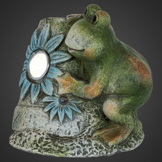Frosch aus Keramik mit integrierter LED‑Solar‑Leuchte, 12 cm hoch, seitliche Ansicht: dekorativer grün‑natürlicher Keramikfrosch lehnt an einem steinähnlichen Element mit geprägten Blüten und runder Solar‑LED.