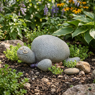 Dekofigur Schildkröte aus Polyresin im Stein-Design, naturgetreu gestaltet mit rundem Panzer und großen Augen, liegt auf Erde zwischen kleinen Pflanzen und Steinen in einem blühenden Gartenbeet.