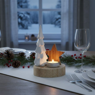 Kerzenhalter für ein Teelicht auf rundem Holzsockel mit Motiv „Baum mit Stern“, auf einem festlich gedeckten Tisch platziert. Neben einem weißen, stilisierten Tannenbaum steht ein Holzstern hinter einem Teelicht in Metallhalterung, dessen warmes Licht die Szene beleuchtet. Im Hintergrund sind Teller, Besteck und Gläser sowie Tannenzweige mit Zapfen und roten Beeren zu sehen; durch ein Fenster erscheint eine verschneite Winterlandschaft.