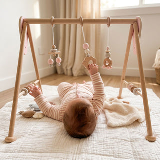 "Baby spielt auf dem Rücken mit Spielbogen 'Schäfchen' in Rosa auf weicher Krabbeldecke – fröhlicher Entdeckungsmoment im hellen Kinderzimmer"