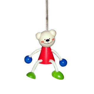 Bunte Schwingfigur in Form eines Bären: Holzfigur mit rundem, naturfarbenem Kopf und aufgemaltem Gesicht, rotem Körper sowie beweglichen Armen und Beinen aus Schnur. Hände sind blau, Füße grün. Oben ist eine Metallfeder zur Aufhängung befestigt. Höhe etwa 11 cm.
