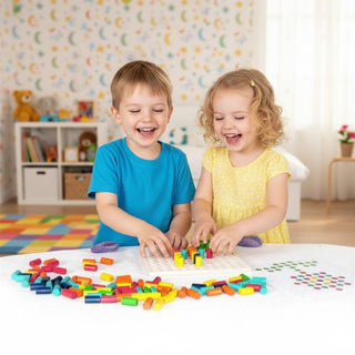 Zwei kleine Kinder sitzen an einem Tisch in einem hellen Kinderzimmer und spielen mit einem Farbensteckspiel. Sie stecken bunte Stäbchen in eine Holzplatte Steckplatte, während zahlreiche farbige Steckteile auf dem Tisch verteilt liegen. Im Hintergrund sind ein Regal mit Spielzeug und Büchern sowie eine dekorierte Wand mit bunten Mond- und Sternmotiven zu sehen.