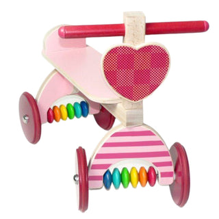 Holz‑Lauflernfahrzeug in Fahrradform mit rosa Lackierung, rotem Lenker, Herzmotiv am Rahmen, bunten Holzperlen und vier Rädern auf weißem Hintergrund.