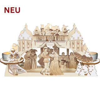 Kerzenhalter „Drei Haselnüsse für Aschenbrödel®“ aus hellem Holz mit Raureifeffekt und farbigen Akzenten. Die detailreiche Szenerie zeigt Aschenbrödel und den Prinzen beim Tanz vor einer Schlosskulisse mit Musikanten, Hofgesellschaft, Haselnüssen, Eule Rosalie und verschneiten Tannen. Drei Teelichthalter sorgen für eine stimmungsvolle, warme Beleuchtung. Breite 24 cm.