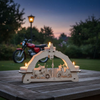 Kerzenhalter für 3 Teelichte „Moped“, 23 cm, aus naturbelassenem Holz mit filigran gelaserten Motiven von Mopeds und einem Fernsehturm, auf einem Holztisch im Garten platziert, im Hintergrund ein stehendes Motorrad, eine Laterne und Bäume bei Dämmerung, mit warm leuchtenden Teelichtern.