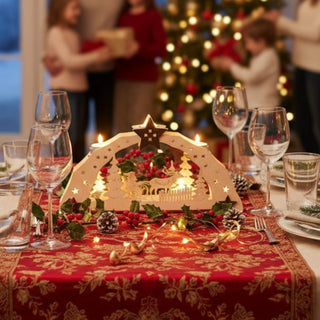 Kerzenhalter für 5 Teelichte „Weihnachtsmann“, 38 cm, aus naturbelassenem Holz mit filigraner Szene mit Weihnachtsmann, Rentier und Tannenbäumen, als festliche Tischdekoration auf einer rot-goldenen Weihnachtstafel mit Gläsern, Tannenzweigen, Zapfen und Lichterkette arrangiert, im Hintergrund ein geschmückter Weihnachtsbaum und Personen beim Geschenkeüberreichen.