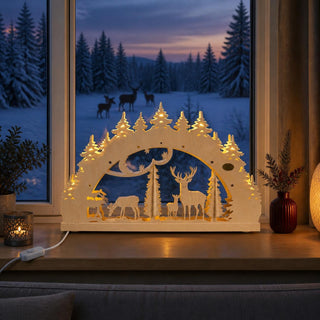 LED-Schwibbogen „Wildfütterung“ aus naturfarbenem Holz mit winterlicher Waldszene in filigraner 3D-Optik. Das Motiv zeigt einen Hirsch, Rehe und eine Futterraufe zwischen Tannenbäumen. Die integrierte warmweiße LED-Beleuchtung hebt die detailreichen Waldmotive hervor und sorgt für eine gemütliche Atmosphäre. Der 52 cm breite Schwibbogen steht auf einer Fensterbank vor einer verschneiten Winterlandschaft in der Dämmerung und verbreitet festliche Weihnachtsstimmung.