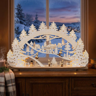 LED Schwibbogen „Wintertraum“ mit filigraner Winterlandschaft aus verschneiten Tannen, Dorfkirche und kleinen Holzfiguren. Der 68,5 cm breite Lichterbogen ist mit warmweißen LEDs beleuchtet und sorgt durch den dekorativen Raureifeffekt für eine besonders winterliche Atmosphäre. Die detailreiche Szene schafft eine stimmungsvolle Weihnachtsdekoration.