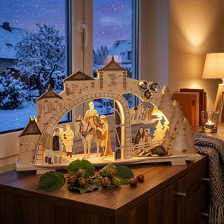 LED Premium-Line-Schwibbogen „Drei Haselnüsse für Aschenbrödel®“ Limited Edition 2025 aus Holz mit beleuchteten Figuren und winterlichen Motiven. Der Schwibbogen steht auf einer Kommode vor einem verschneiten Fenster und strahlt warmes Licht aus.