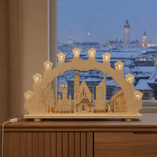 LED-Schwibbogen „Leipzig“ aus naturfarbenem Holz, 66 cm breit. Der beleuchtete Bogen zeigt eine detailreiche Silhouette bekannter Leipziger Wahrzeichen und Stadtmotive. Warmweiße LED-Lichter in laternenförmigen Aufsätzen sorgen für eine stimmungsvolle Beleuchtung. Der Schwibbogen steht auf einer Fensterbank vor einer winterlichen Stadtkulisse und schafft eine festliche Weihnachtsatmosphäre.