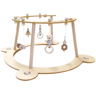 Ein hölzernes Baby-Spielgerät mit einer runden Basis und vier Beinen. Von der oberen Stange hängen verschiedene Spielzeuge, darunter ein Bär, Ringe und Perlen. Die Struktur ist so gestaltet, dass Säuglinge darunter liegend spielen können.
