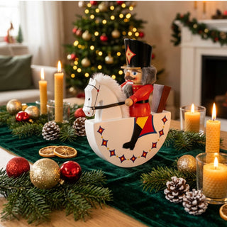 Nussknacker „Reiterlein“ (29 cm) in Rot als Schaukelpferd-Figur, dekorativ auf einem festlich gedeckten Tisch mit Kerzen, Tannenzweigen und Weihnachtskugeln vor geschmücktem Weihnachtsbaum platziert.