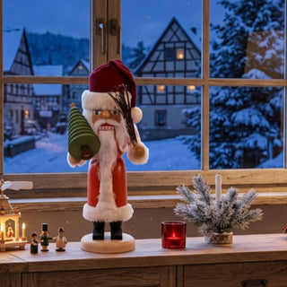 Nussknacker „Weihnachtsmann“ (36 cm) in Rot mit Tannenbaum, stehend auf einem Holzsockel, dekorativ auf einer Kommode mit Kerzen und winterlicher Dorfkulisse vor dem Fenster platziert.Geben Sie Ihr Feedback zu BizChat ab.