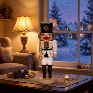 Nussknacker „König“ in weißer Uniform (29 cm) auf einem Tisch, mit Kerze und Weihnachtsdeko vor winterlichem Fenster.