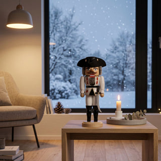 Nussknacker „General“ in weißer Uniform (36 cm) auf einem Tisch, neben einer Kerze, vor winterlichem Fenster mit Schneefall.