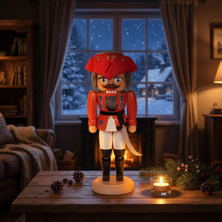 Nussknacker „General“ in roter Uniform (36 cm) auf einem Tisch, mit Kerze und weihnachtlichem Wohnzimmer vor Fenster mit Schneefall.
