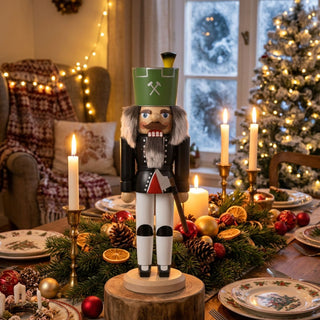 Nussknacker „Bergmann“ (36 cm) in Grün mit Axt, auf einem Holzsockel stehend, dekorativ auf einem festlich gedeckten Tisch mit Kerzen, Tannenzweigen und Weihnachtskugeln vor geschmücktem Weihnachtsbaum platziert.