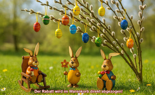 Drei dekorative Hasenfiguren aus Holz sitzen auf einer Wiese unter einem Zweig mit bunten, aufgehängten Ostereiern. Unten steht der Text: „Der Rabatt wird im Warenkorb direkt abgezogen!“.
