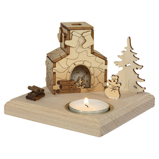 Holzdeko in Form eines kleinen Räucherhauses „Kamin“ auf einer Holzplatte, mit Weihnachtsbaum, Geschenkesack, Holzscheiten und einem Teelicht.