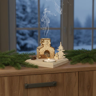 Kerzenhalter für 1 Teelicht mit Räucherhaus „Kamin“, 9 cm, aus naturbelassenem Holz mit detailreichem kleinen Haus mit Schornstein und Räucherfunktion, dekorativ auf einem Holzsideboard mit Tannenzweigen platziert, vor einem Fenster mit verschneiter Winterlandschaft, während zarter Rauch aus dem Schornstein aufsteigt und ein Teelicht für warmes Licht sorgt.