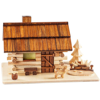 Räucherhaus aus Holz in Form eines Garten-Blockhauses mit braunem Schindeldach, Schornstein und Vordertür. Holzstücke, ein Hund und einem kleinen Baum sind zu sehen. Alles steht auf einer rechteckigen Holzplatte.
