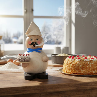 Räuchermännchen „Kuchenbäcker“ (12 cm), farbig gestaltet mit Kochmütze, Schnurrbart und Kuchen in der Hand, rauchend auf einem Tisch in heller Küche mit Backzutaten und Torte dekoriert.