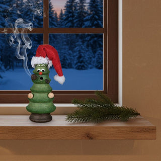 Räuchermännchen „Weihnachtswichtel“ (14 cm), farbig gestaltet als kleine Tanne mit roter Mütze, rauchend auf einer Fensterbank vor winterlicher Abendkulisse dekoriert.